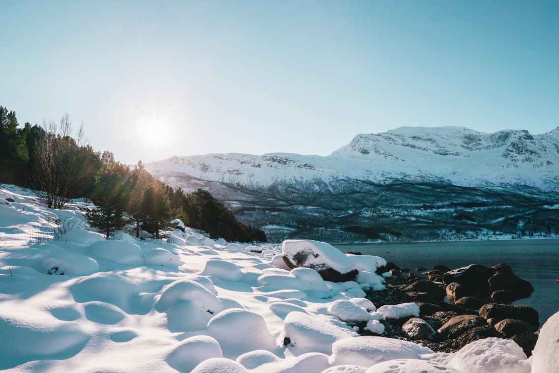 snow covered rocks on shore near hill