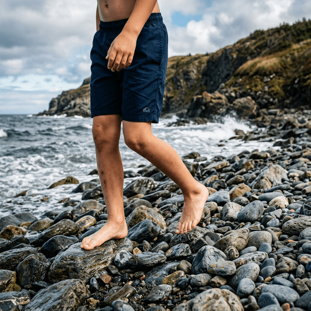 Child walking barefoot across rocks beside a rugged ocean shoreline